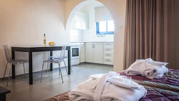 Habitación de hotel con cama, escritorio, silla y una cocina visible a través de un arco. Toallas sobre la cama.