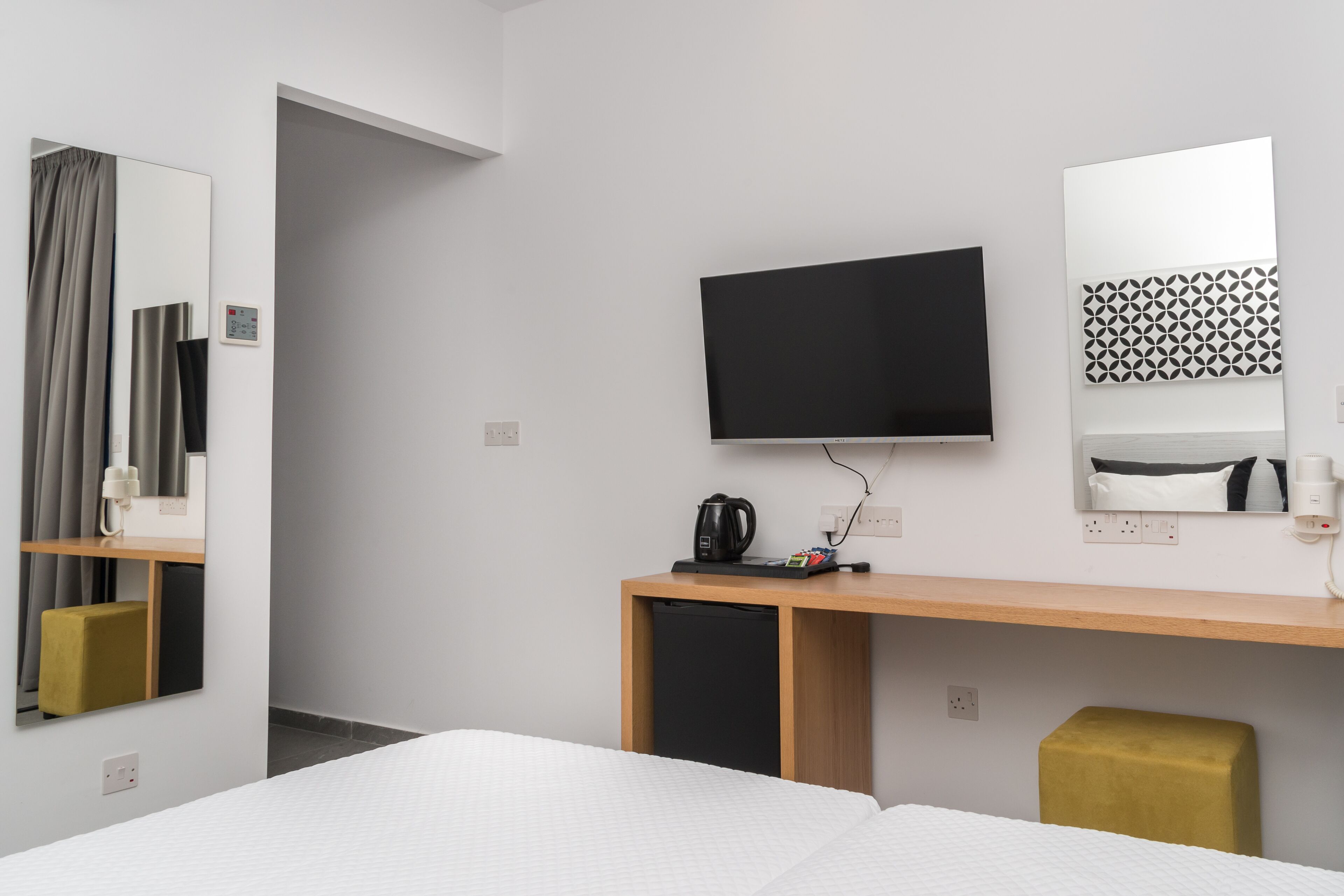 A hotel room with a bed, a TV, a desk with a coffee maker, a mirror, and a patterned wall decoration.