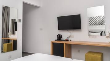 A hotel room with a bed, a TV, a desk with a coffee maker, a mirror, and a patterned wall decoration.