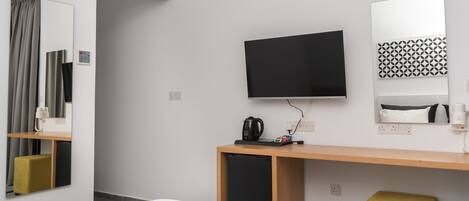 A hotel room with a bed, a TV, a desk with a coffee maker, a mirror, and a patterned wall decoration.