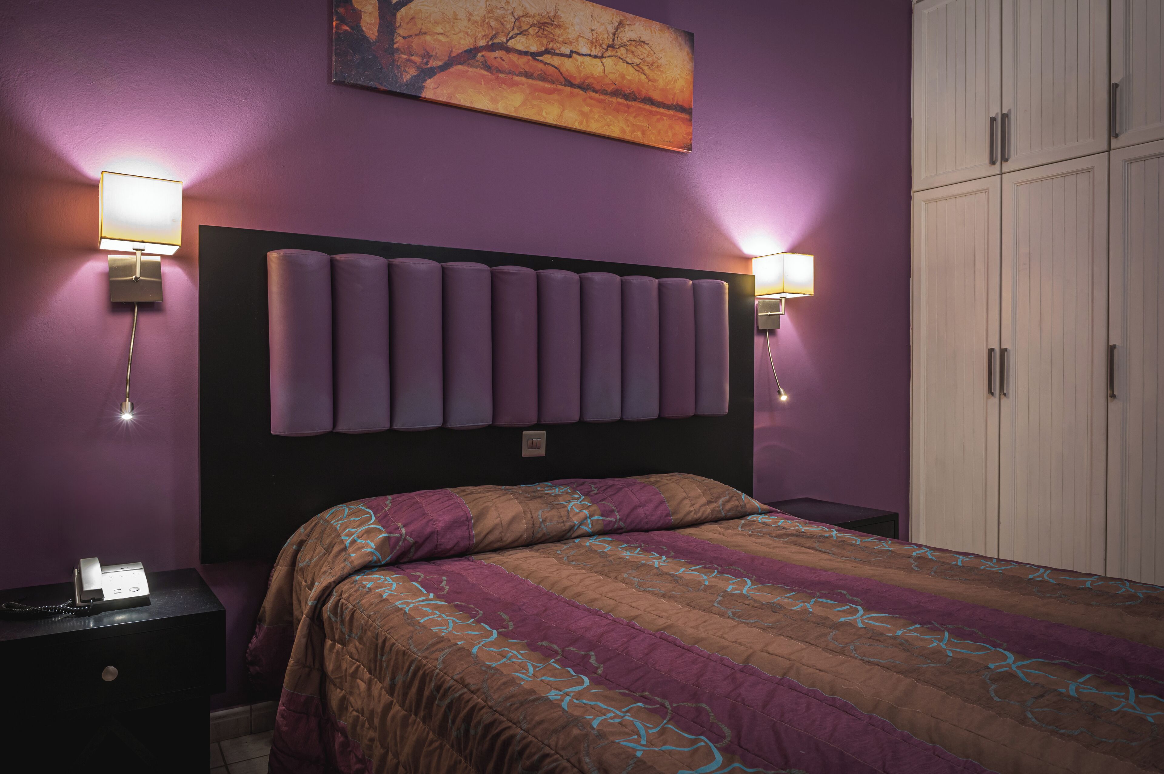 Ein Schlafzimmer mit einem großen Bett, zwei Nachttischlampen, einem Nachttisch und einem Kleiderschrank.