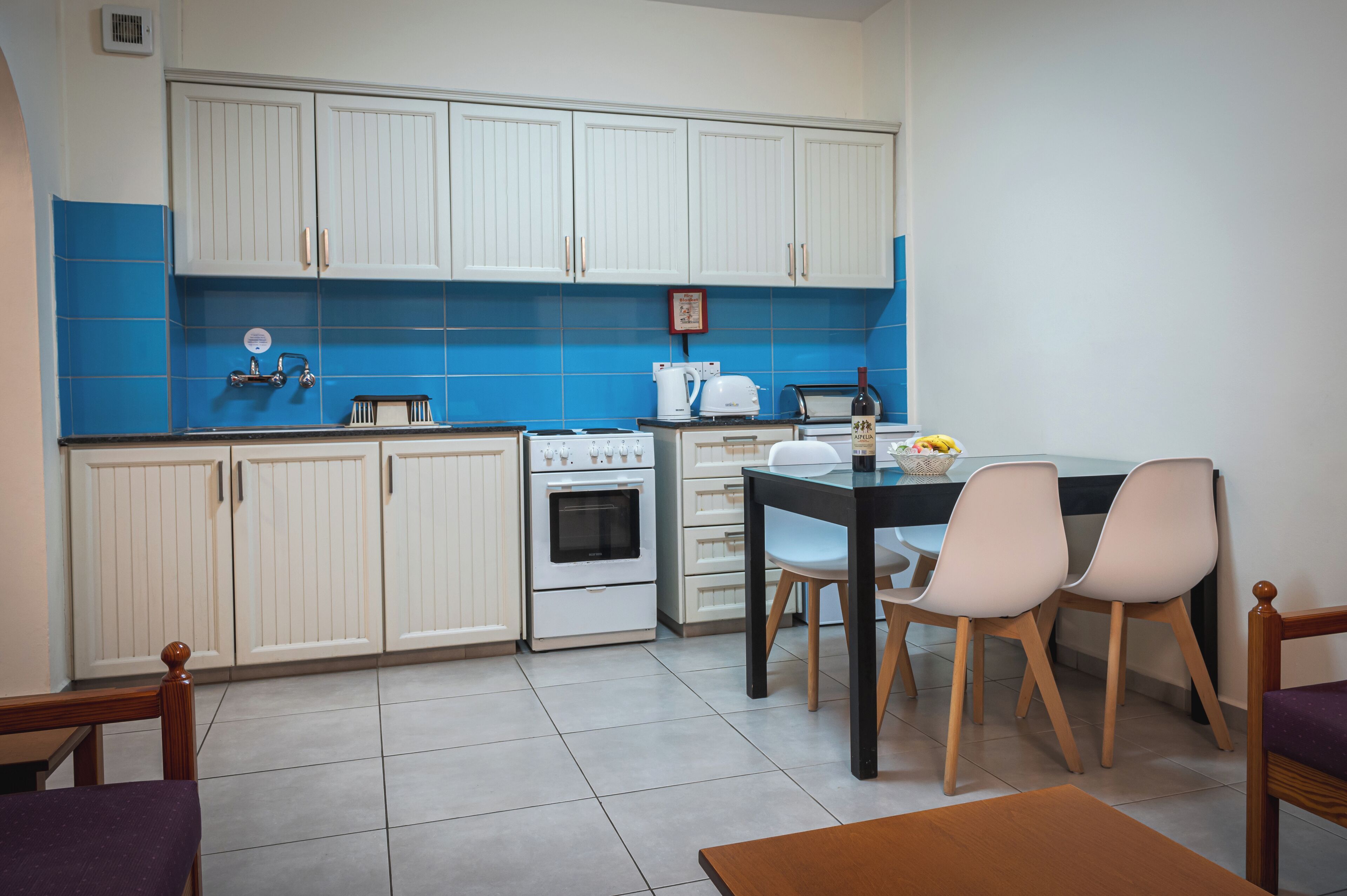 A compact kitchen with white cabinets, a stove, and a dining area with a table and chairs.
