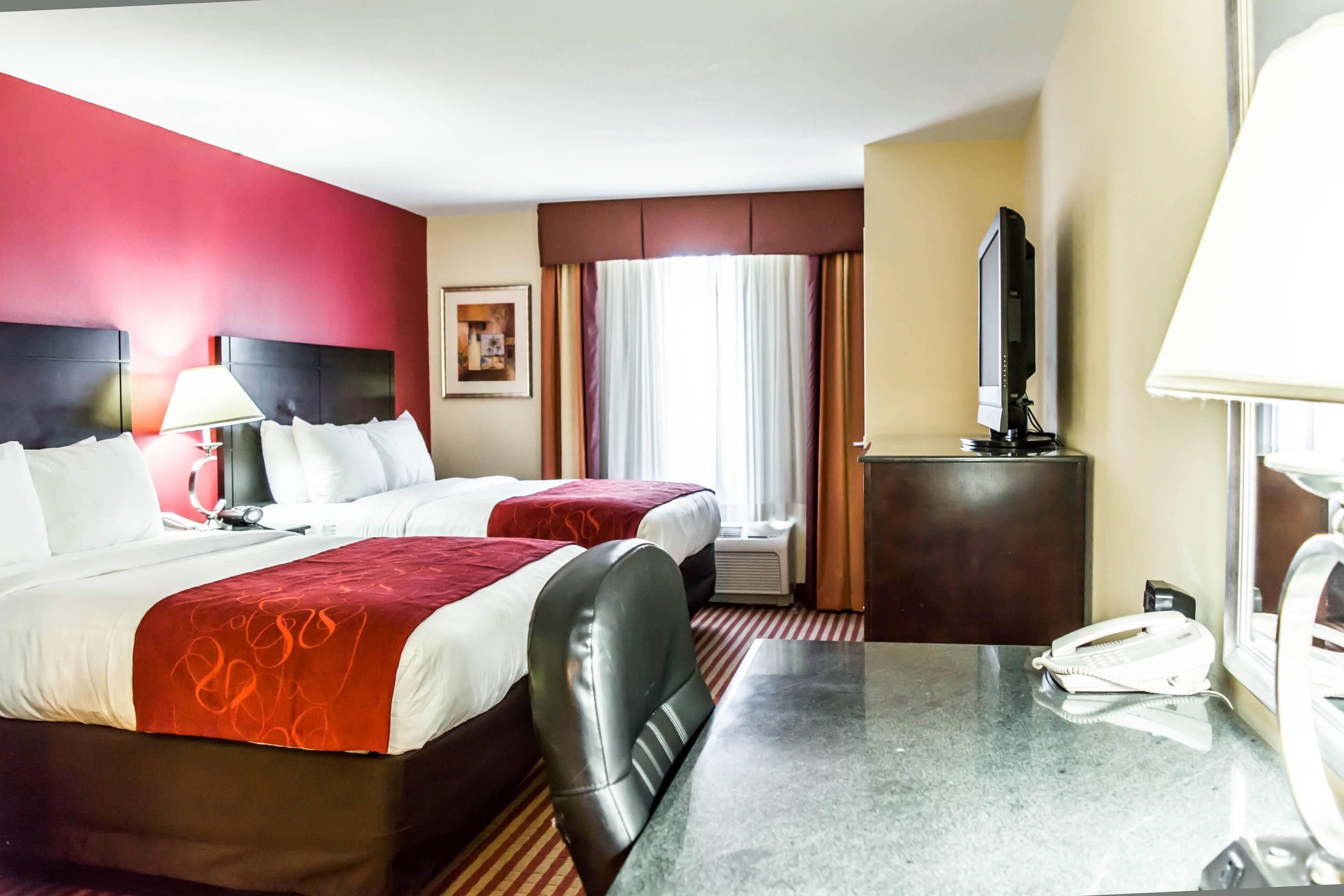 A hotel room with two beds, a desk, a telephone, a television, and a window with curtains.