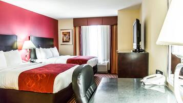 A hotel room with two beds, a desk, a telephone, a television, and a window with curtains.