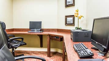 Oficina de hotel con escritorio, dos computadoras, teclado, ratón y una silla.