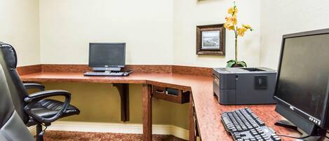 A hotel office with a desk, two computers, a keyboard, a mouse, and a chair.