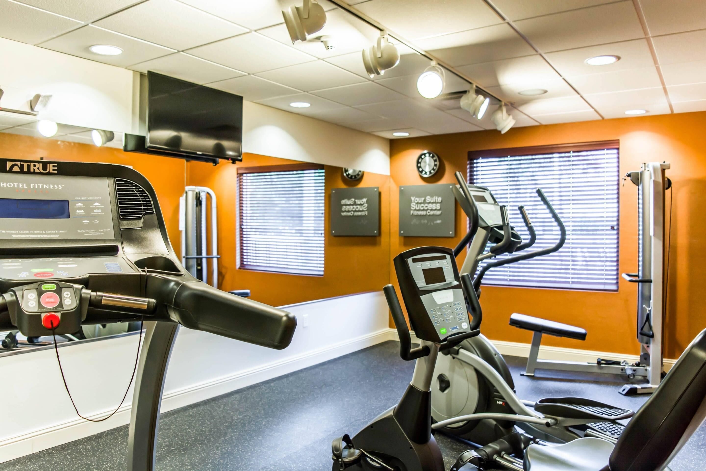A gym with exercise equipment, motivational wall decorations, and a clock.