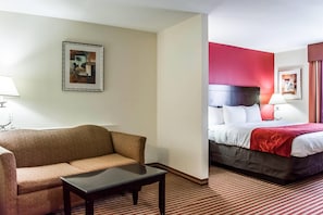 Een hotelkamer met een bank, een kleine tafel, een bed met een rode hoofdbord en een ingelijste foto aan de muur.