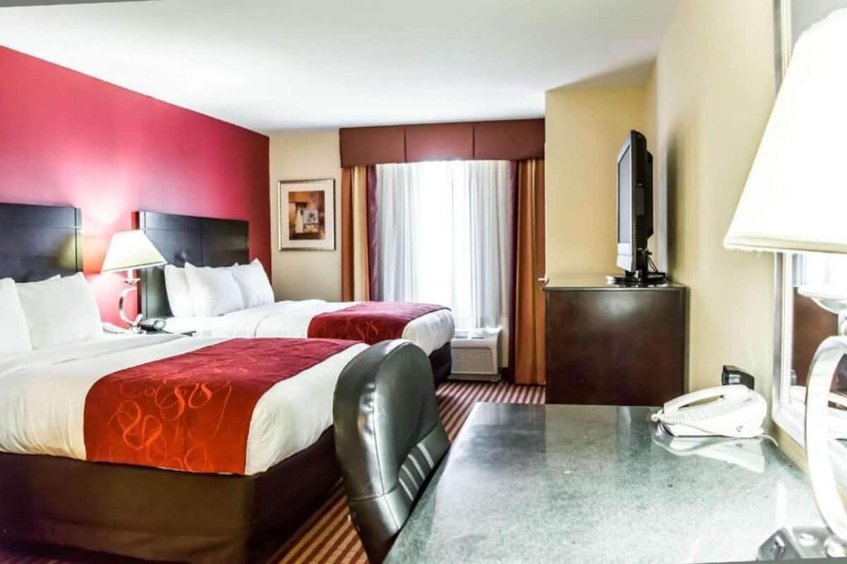Une chambre d’hôtel avec deux lits, un bureau, un téléphone, une télévision et une fenêtre avec des rideaux.