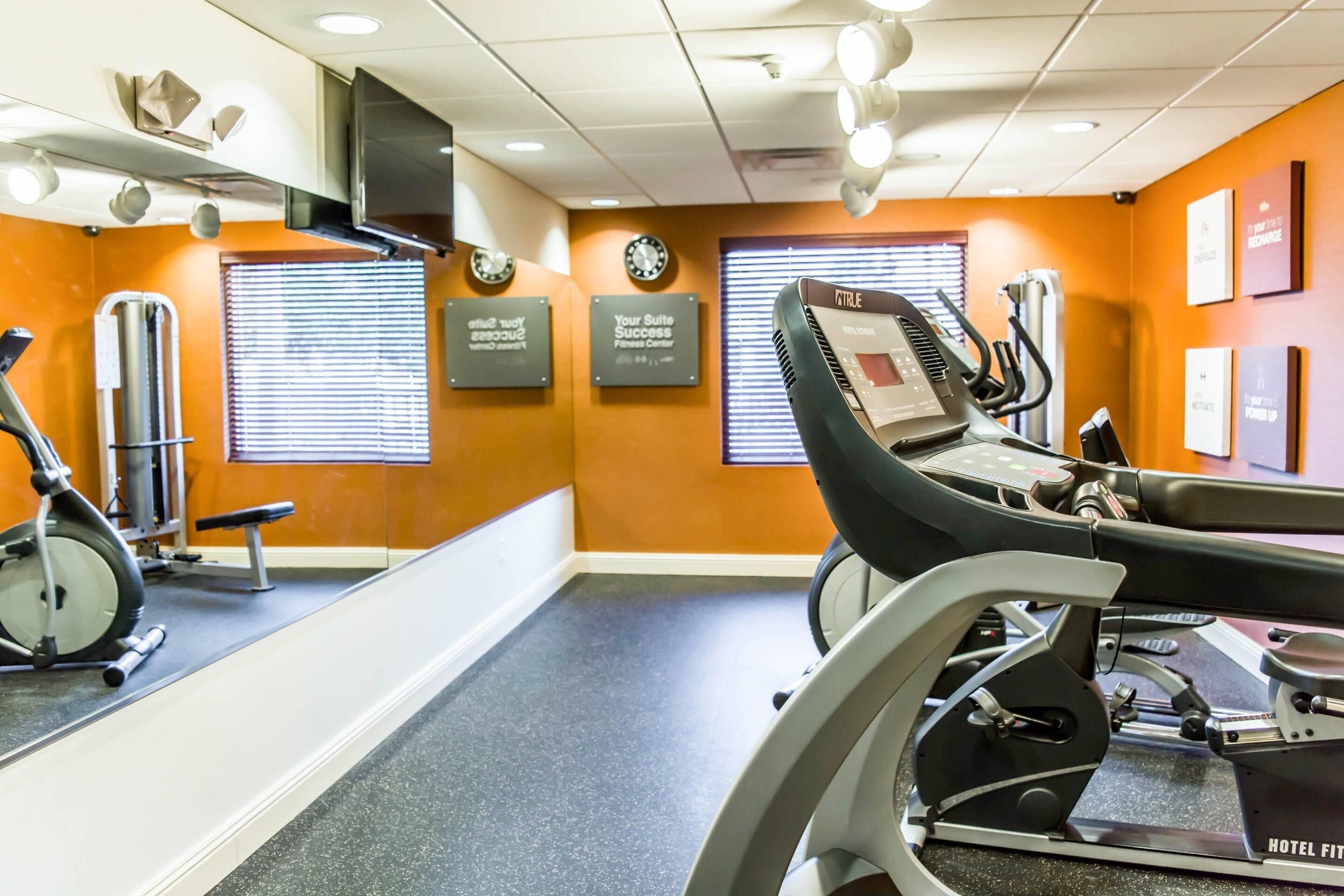 Ein Fitnessraum eines Hotels mit Trainingsgeräten, einer Spiegelwand und motivierenden Schildern.