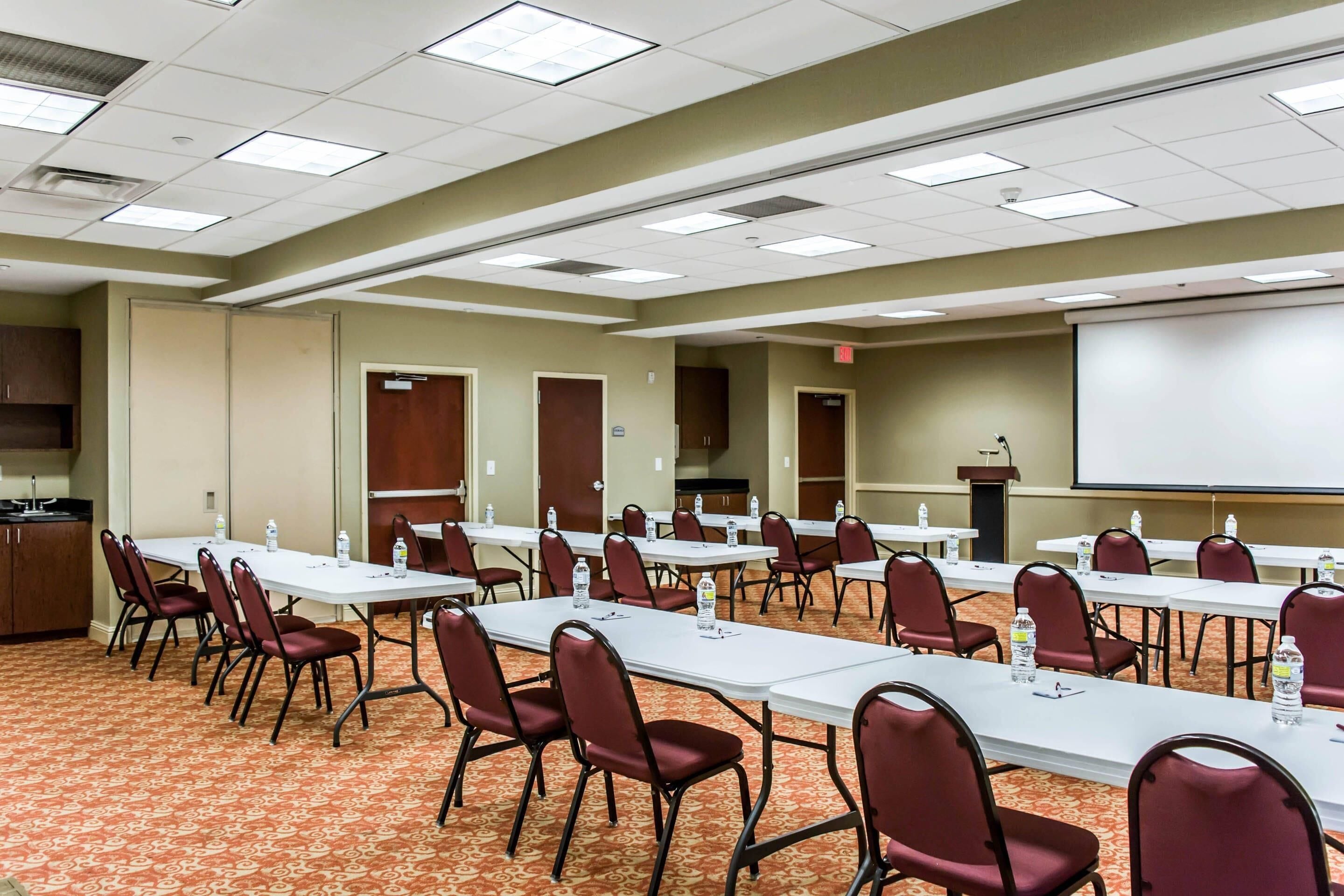A conference room with multiple tables and chairs, a projector screen, and a podium.