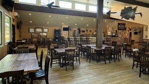 A spacious restaurant with high ceilings, wooden tables and chairs, and a rustic stone wall. - Flying L Ranch Resort (Bandera)