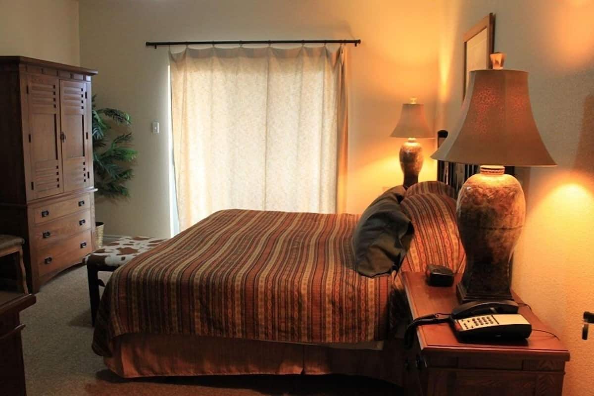 Una habitación de hotel con cama, escritorio con lámpara, teléfono y armario.