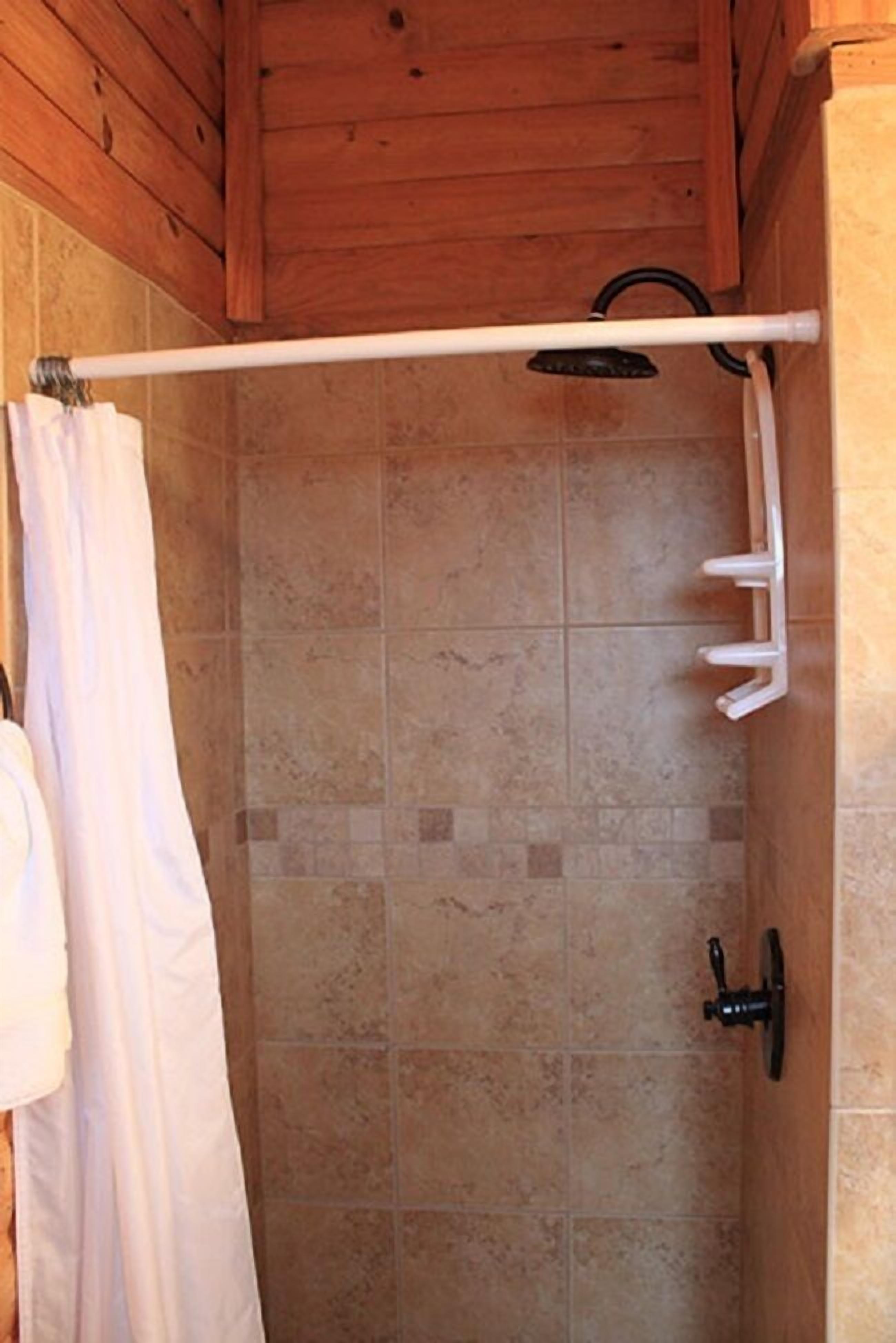 A shower area with tiled walls, a white shower curtain, and a handheld showerhead.