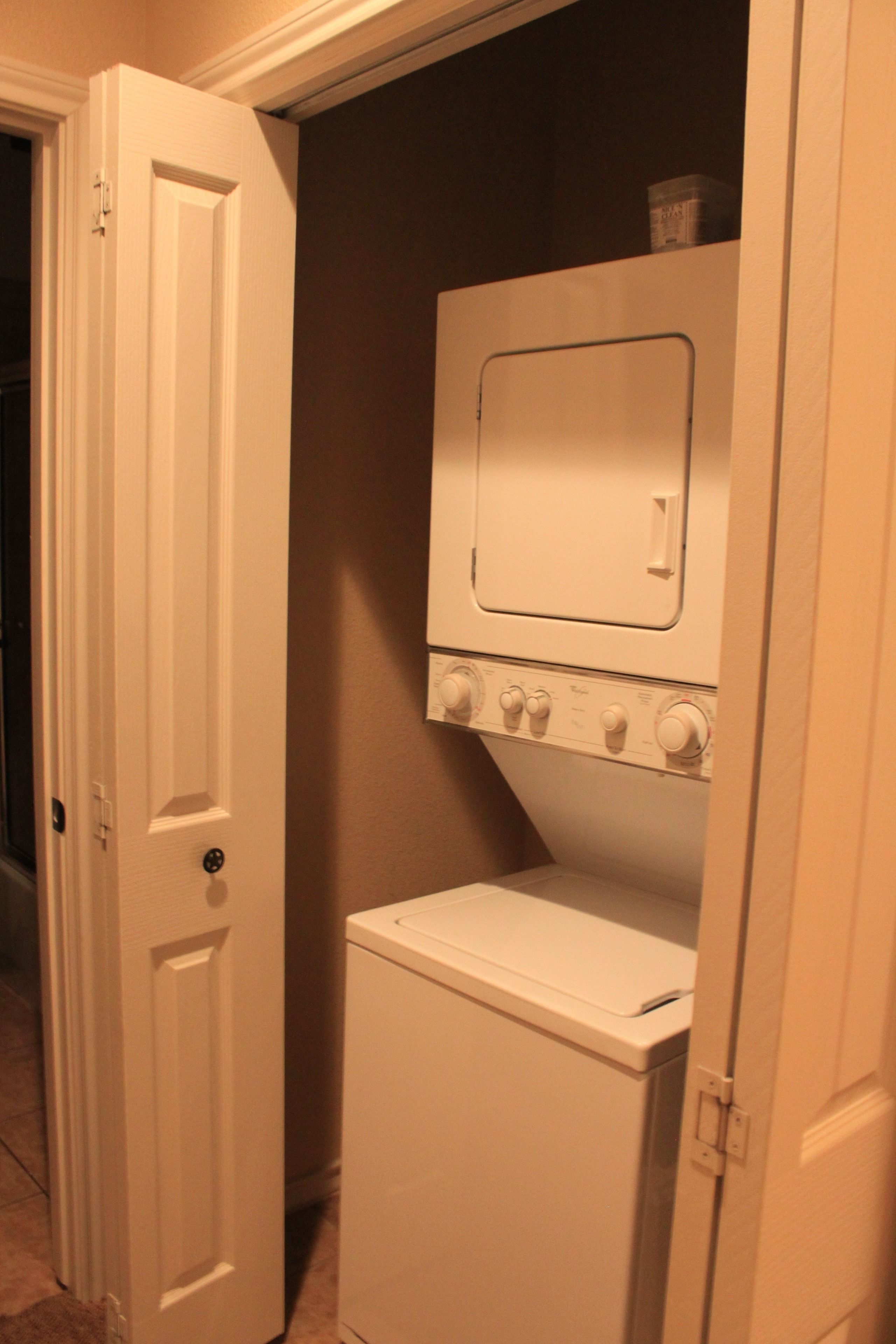 A compact laundry room with a washing machine and dryer, a door, and a shelf above the dryer.