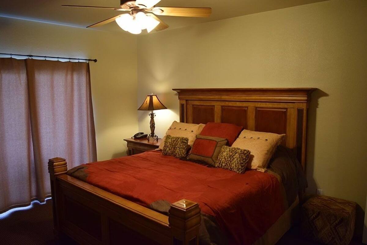 Un dormitorio con cama de madera, una mesita de noche con lámpara y un ventilador de techo.