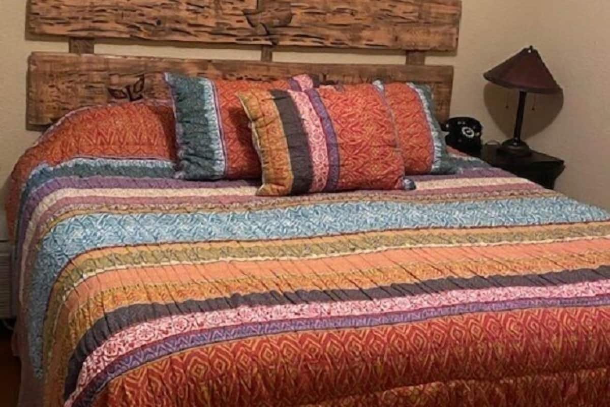 Una cama con cabecera de madera, almohadas coloridas y colcha a rayas.