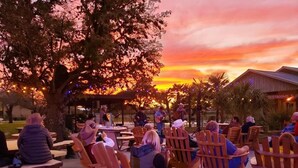 An outdoor seating area with wooden chairs and tables, a stage with musicians, and a sunset in the background. - Flying L Ranch Resort (Bandera)