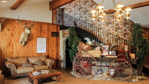 A rustic interior with a wooden staircase, a leather sofa, a wooden coffee table, and a vintage carriage. - Flying L Ranch Resort (Bandera)