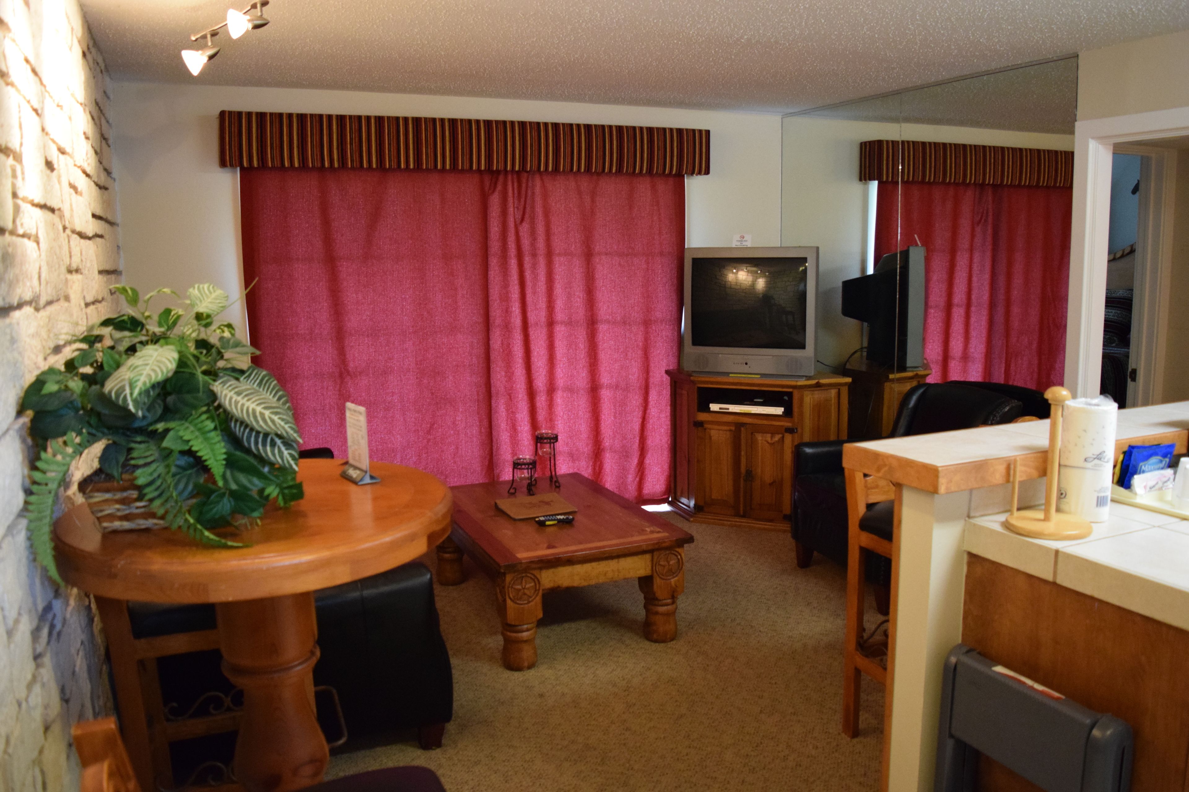 A living room with a brick wall, a wooden table, a TV, and a red curtain.