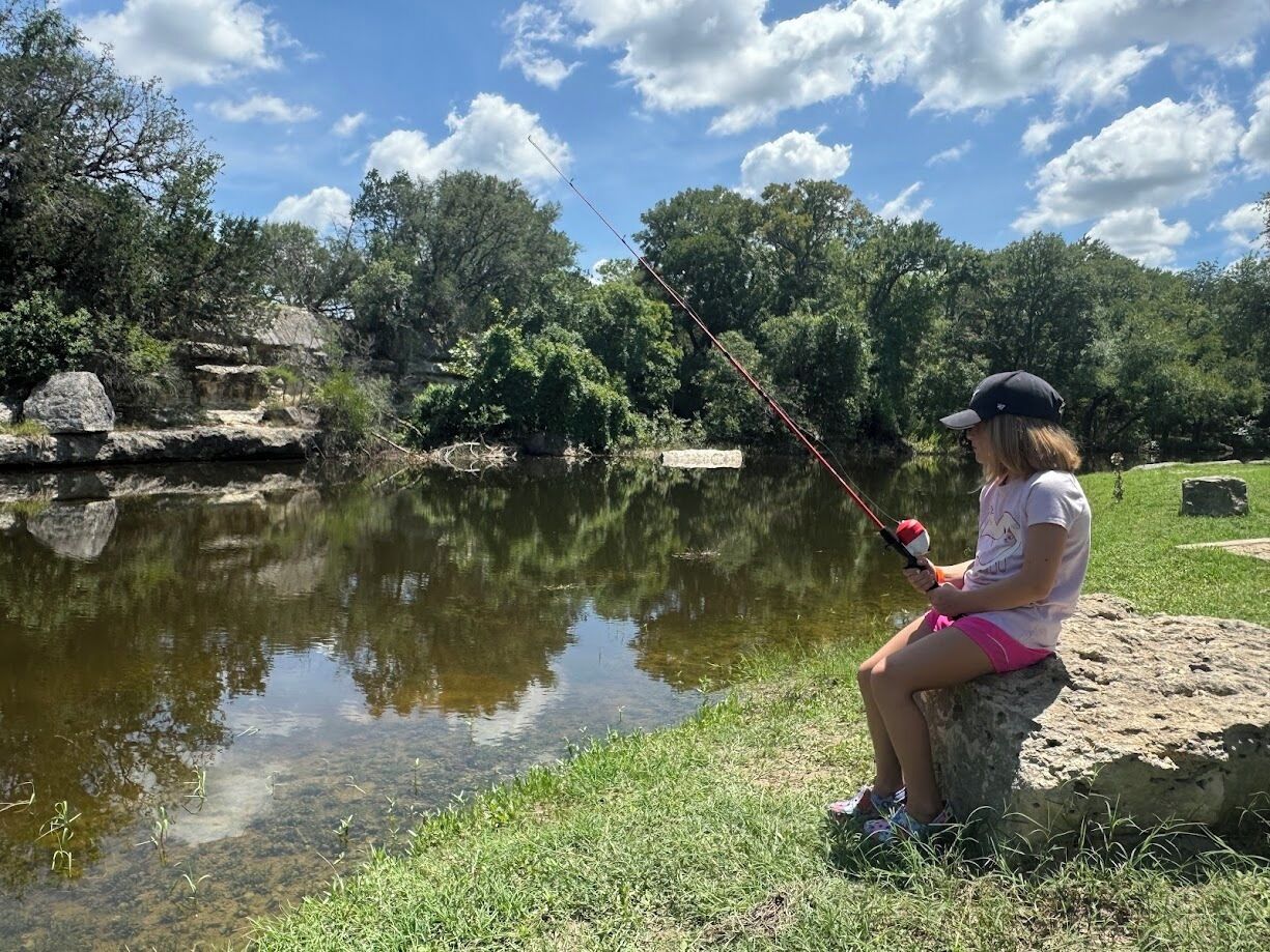A person fishing by a calm lake surrounded by trees.