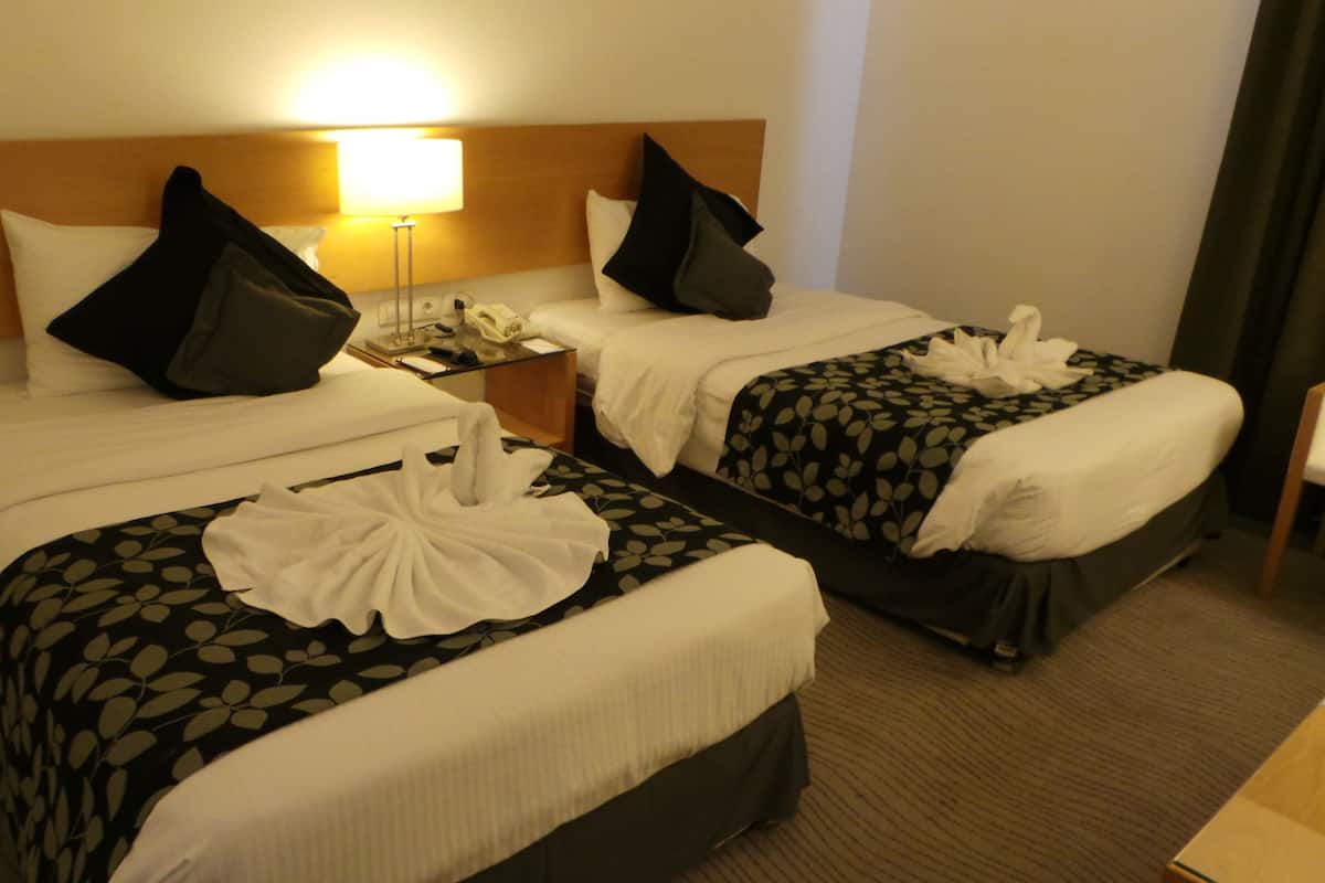 A hotel room with two beds, each with a pillow and a blanket. There is a nightstand with a lamp and a phone.