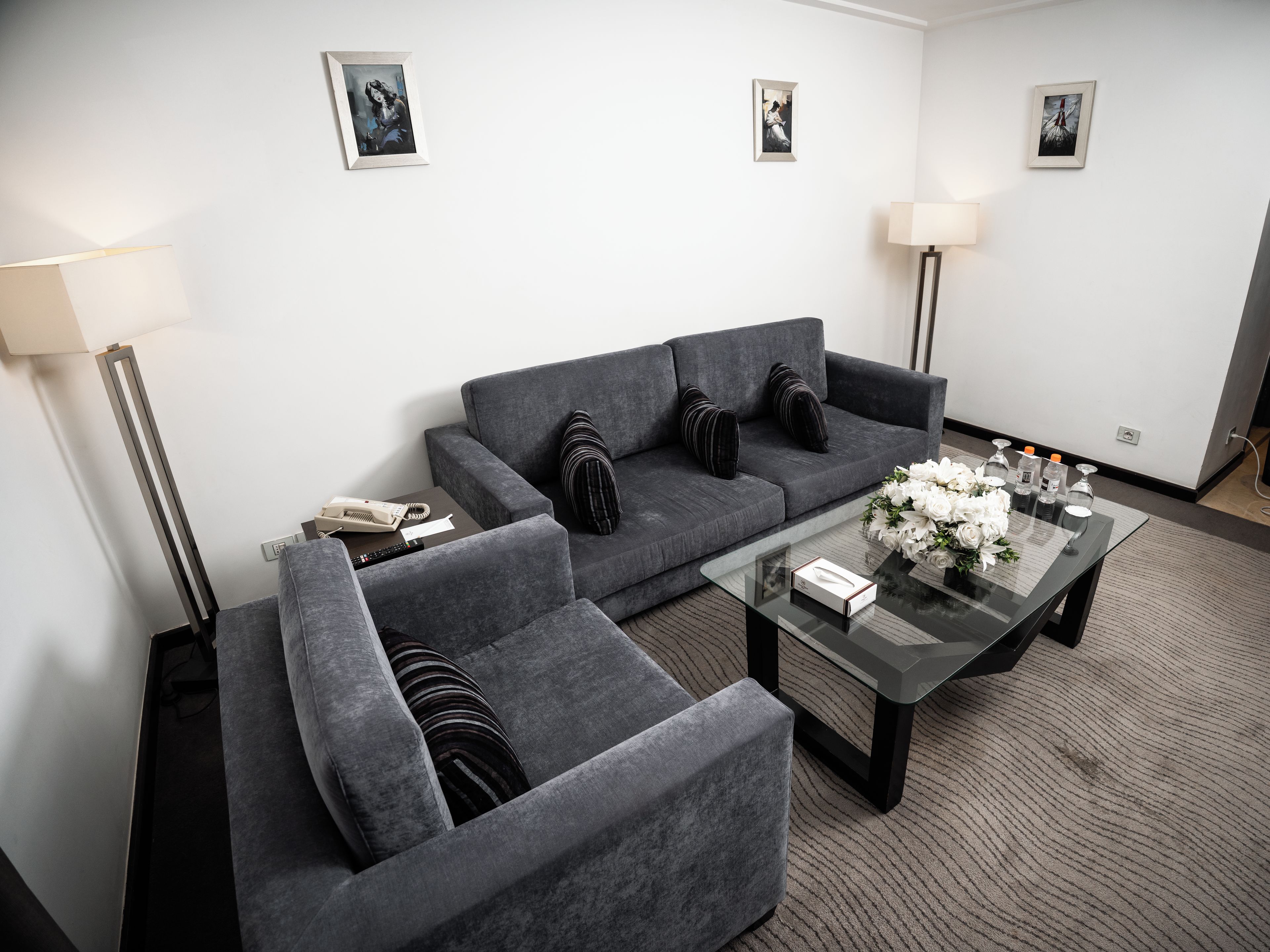 Una sala de estar moderna con un sofá gris, sillones, una mesa de centro de vidrio y un centro de mesa con flores.