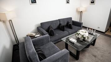 Una sala de estar moderna con un sofá gris, sillones, una mesa de centro de vidrio y un centro de mesa con flores.