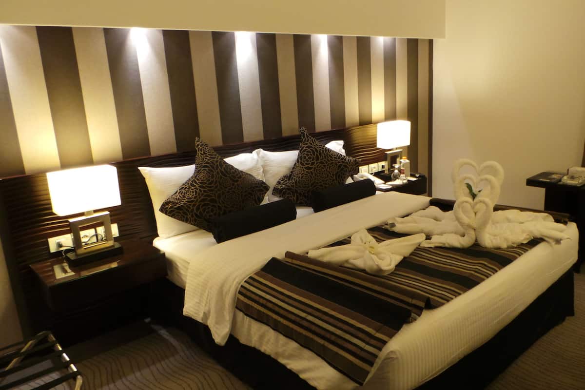 A hotel room with a large bed, striped headboard, two bedside lamps, and a heart-shaped towel arrangement.