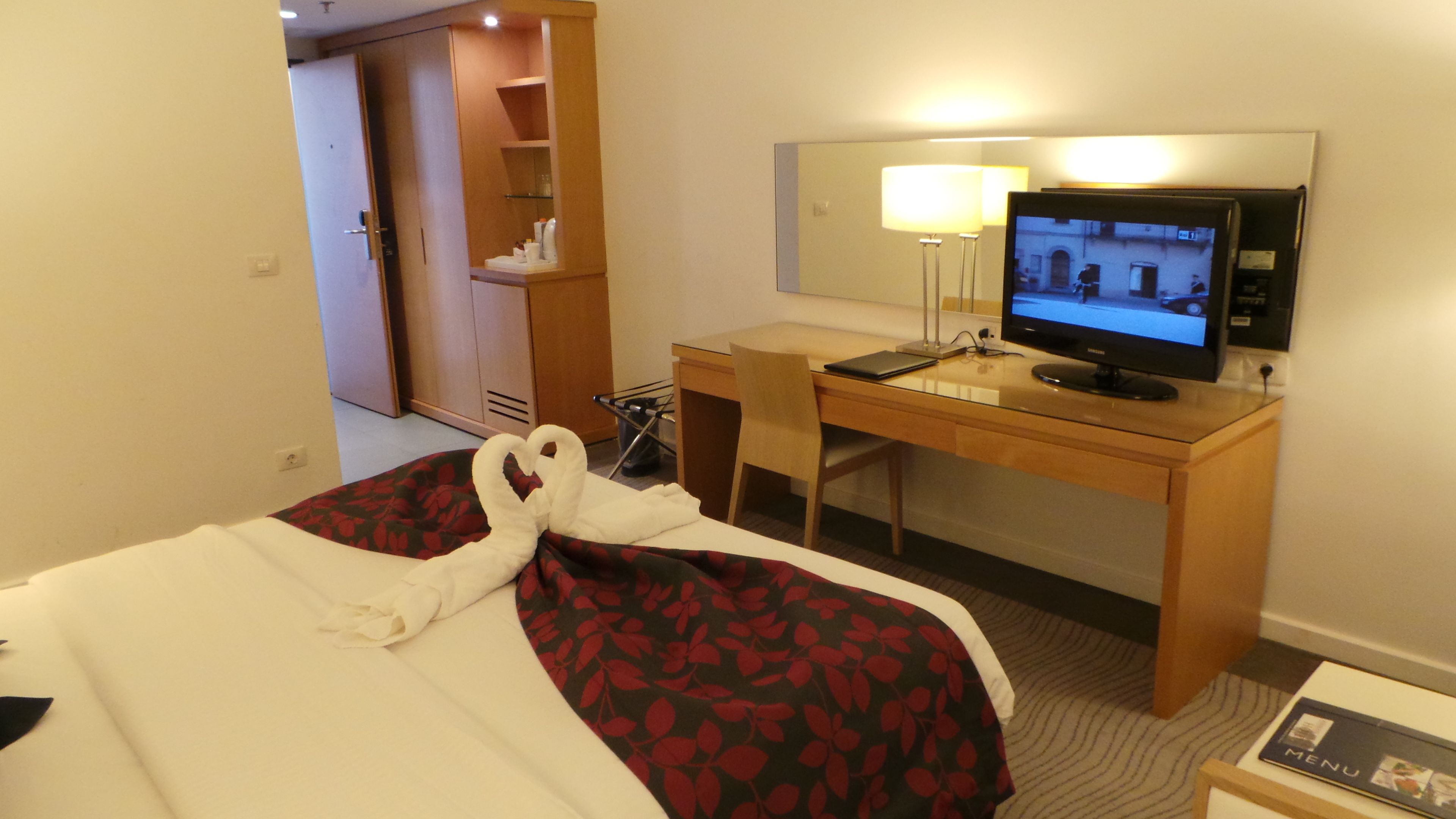 A hotel room with a bed, a desk, a chair, a television, and a wardrobe.