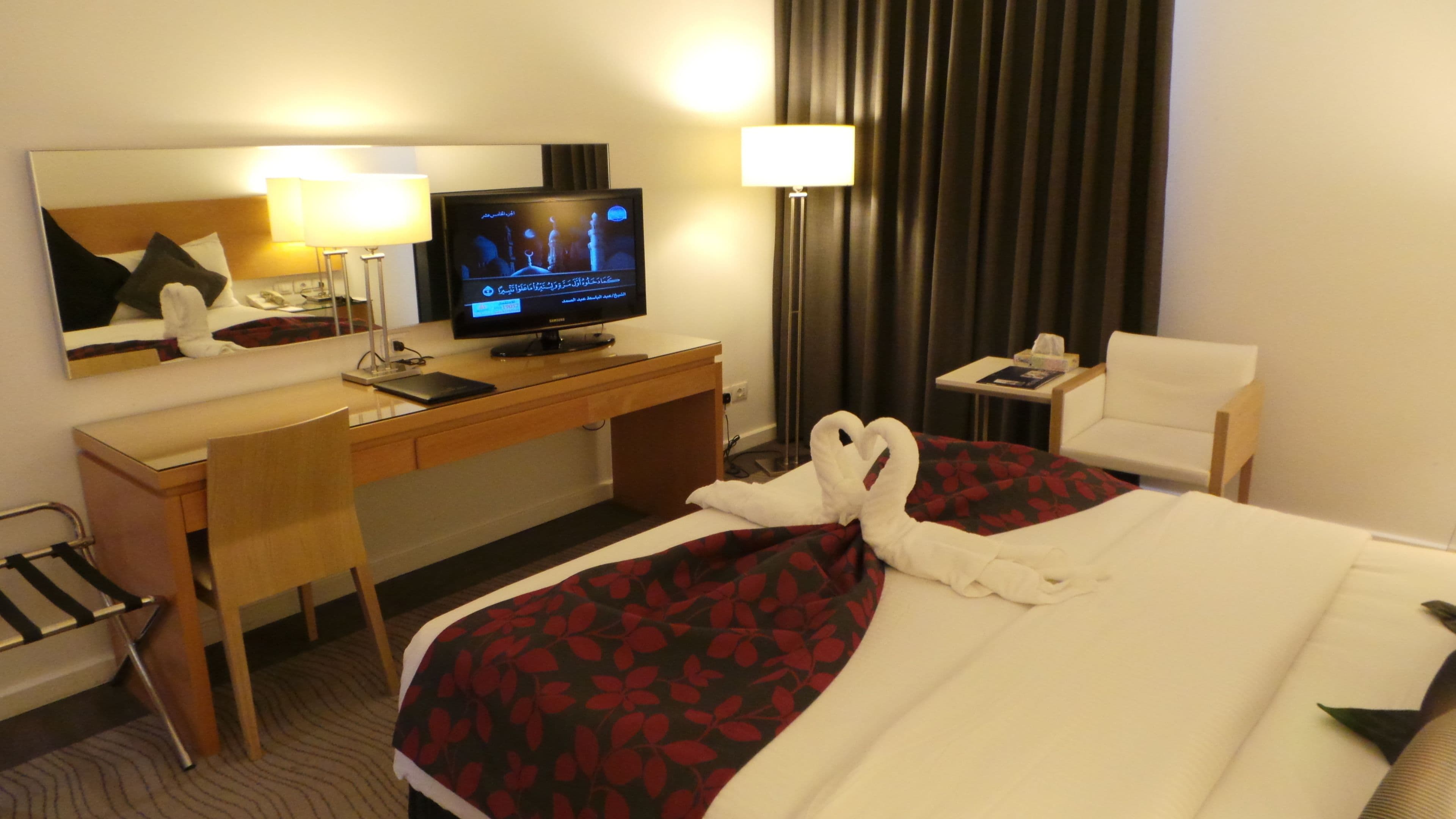 Una habitación de hotel con cama, escritorio, televisor, silla y lámpara.