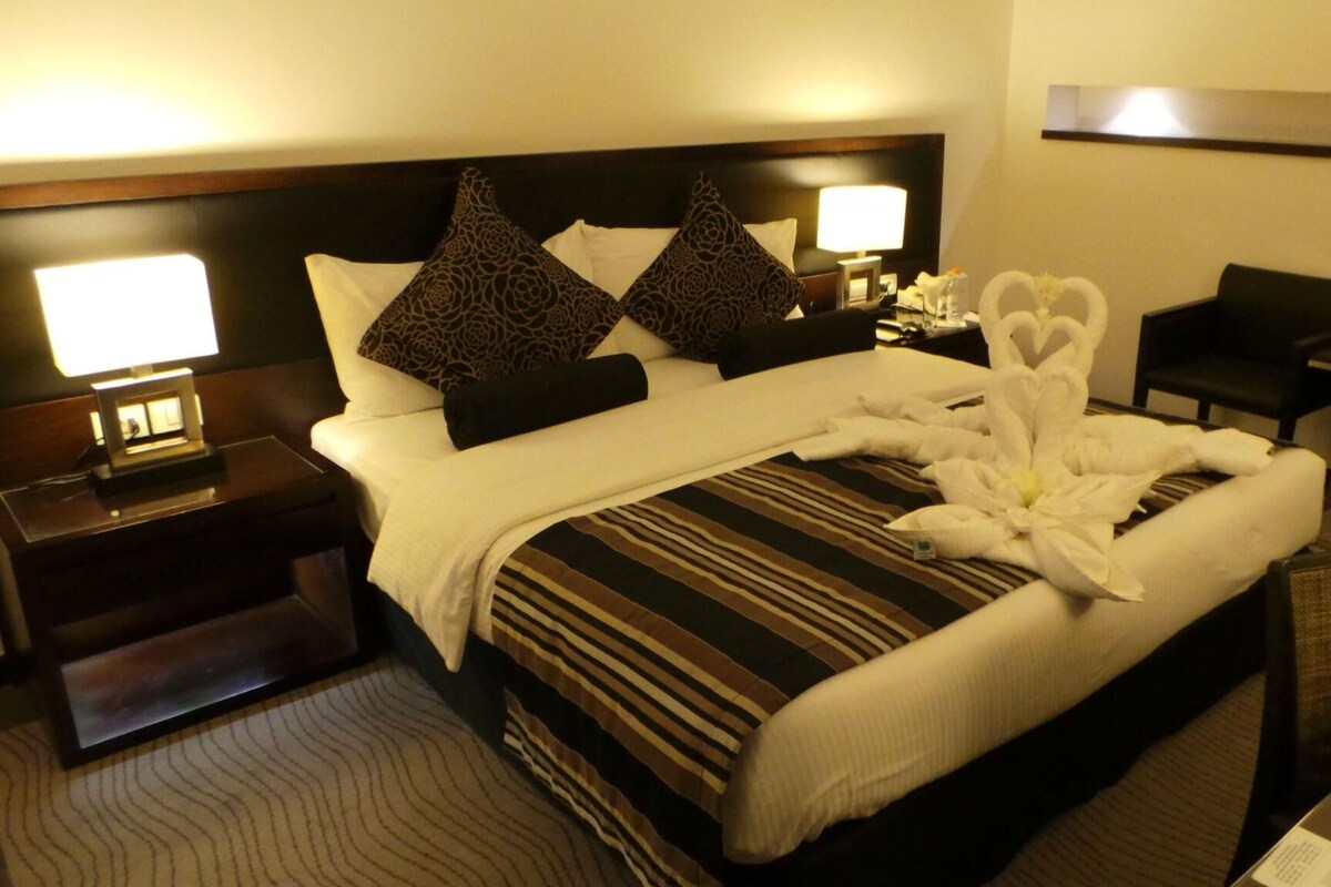 A hotel room with a large bed, two nightstands, a desk, and a chair.