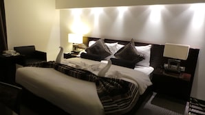 Una habitación de hotel con una cama bien hecha, una mesita de noche con una lámpara y una silla.