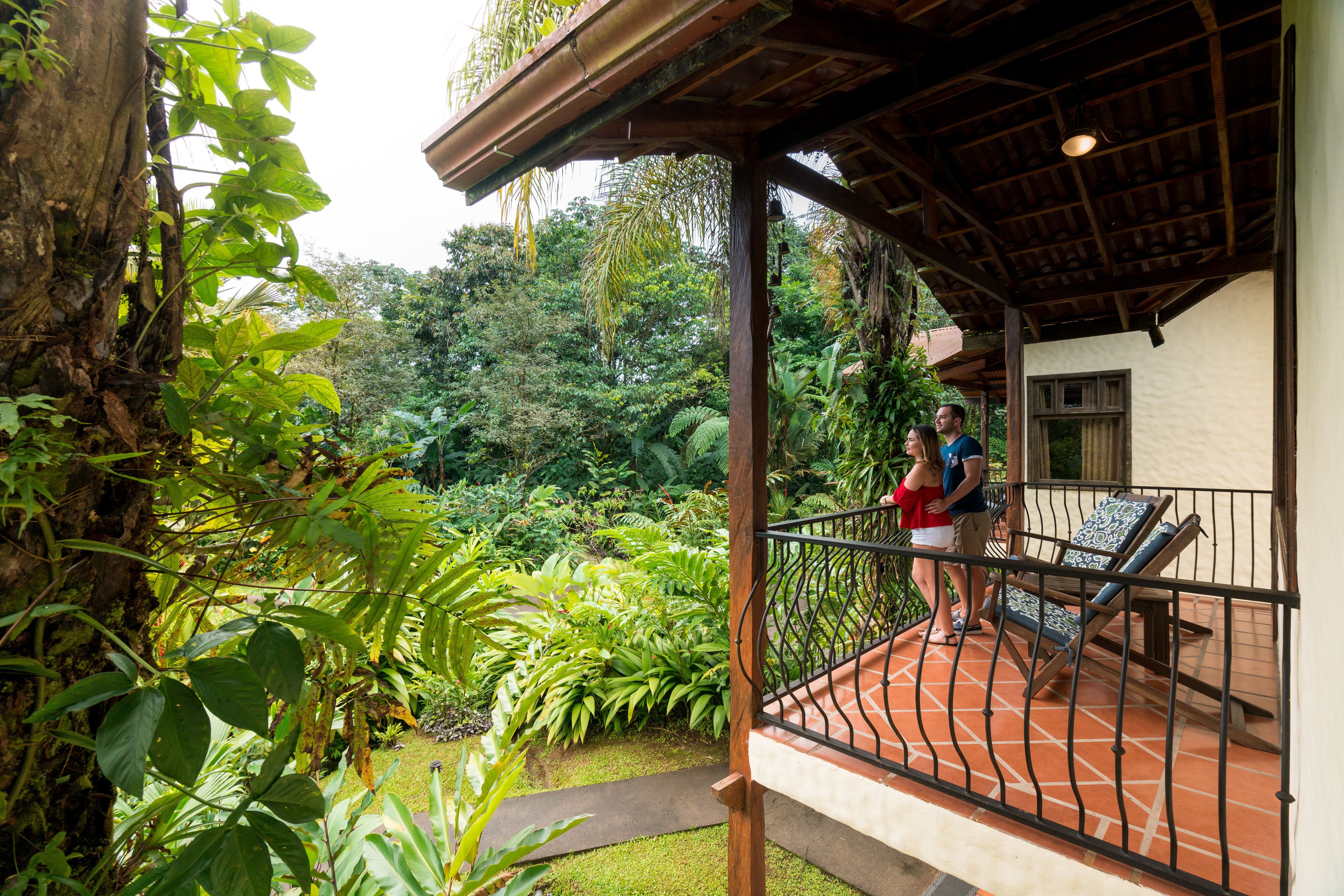 Un espacio al aire libre cubierto con barandilla de madera, un pequeño patio con dos sillones de descanso y abundante vegetación al fondo.