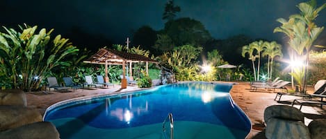Une piscine nocturne avec des chaises longues et un kiosque.