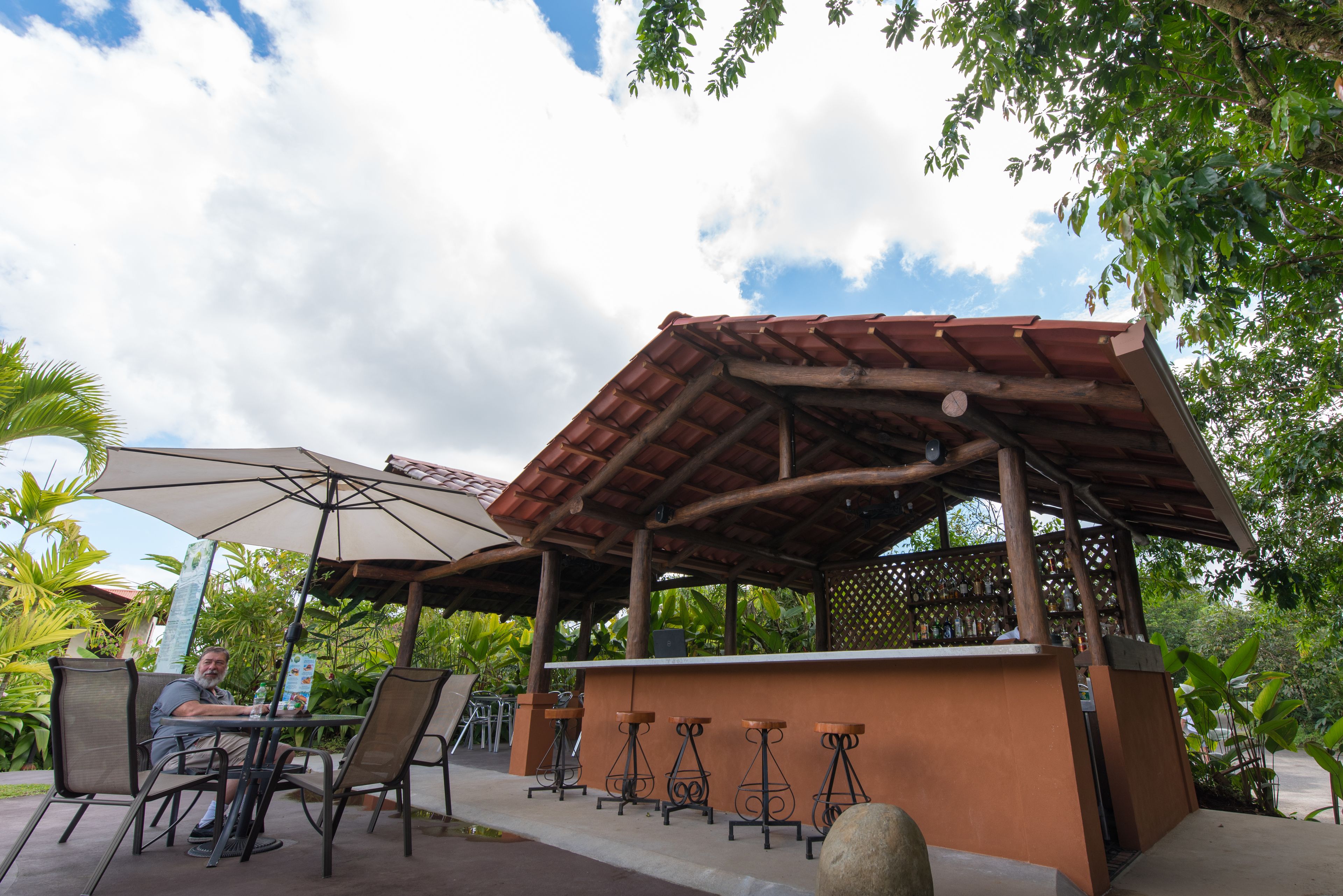 An outdoor seating area with a wooden pergola, a bar counter, and a table with chairs.