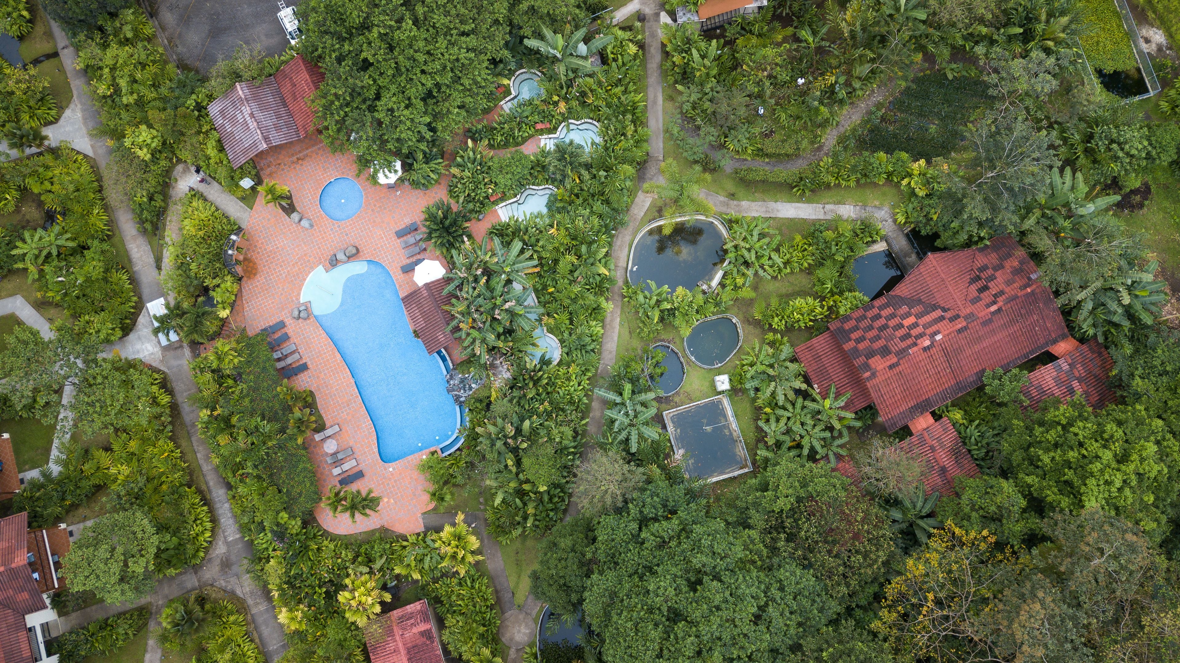 An aerial view of a property with a swimming pool, multiple small ponds, and a red-roofed building.