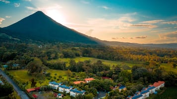 Vista aérea de un resort con varias edificaciones, un volcán al fondo y abundante vegetación.