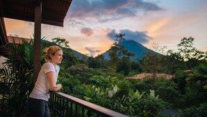 A woman standing on a balcony overlooking a lush garden with a mountain in the background. - Casa Luna Hotel & Spa (La Fortuna)