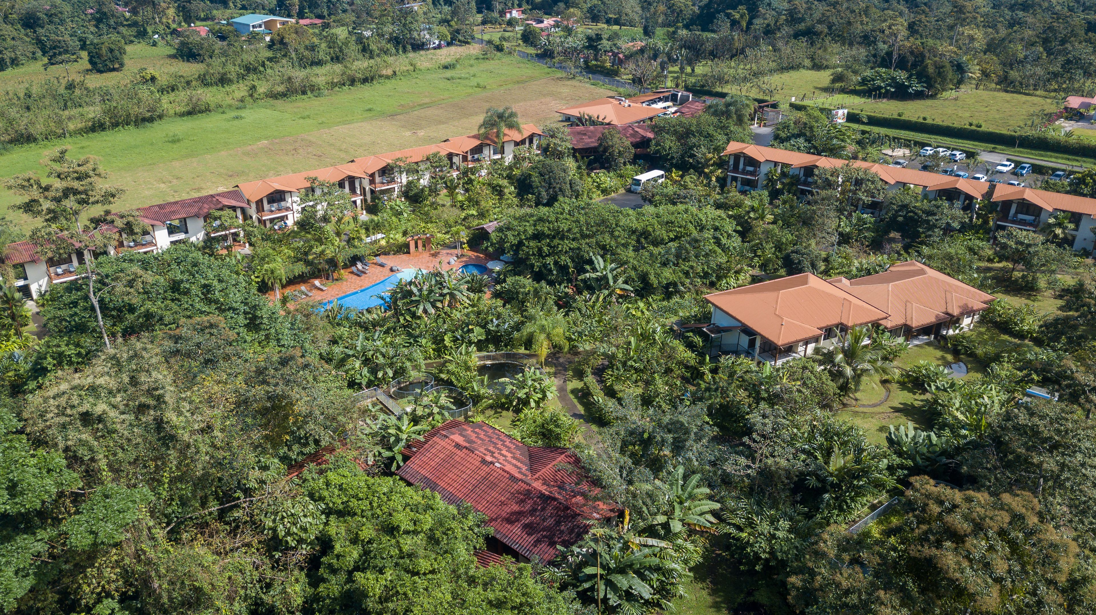 An aerial view of a resort with multiple buildings, a swimming pool, and lush greenery.