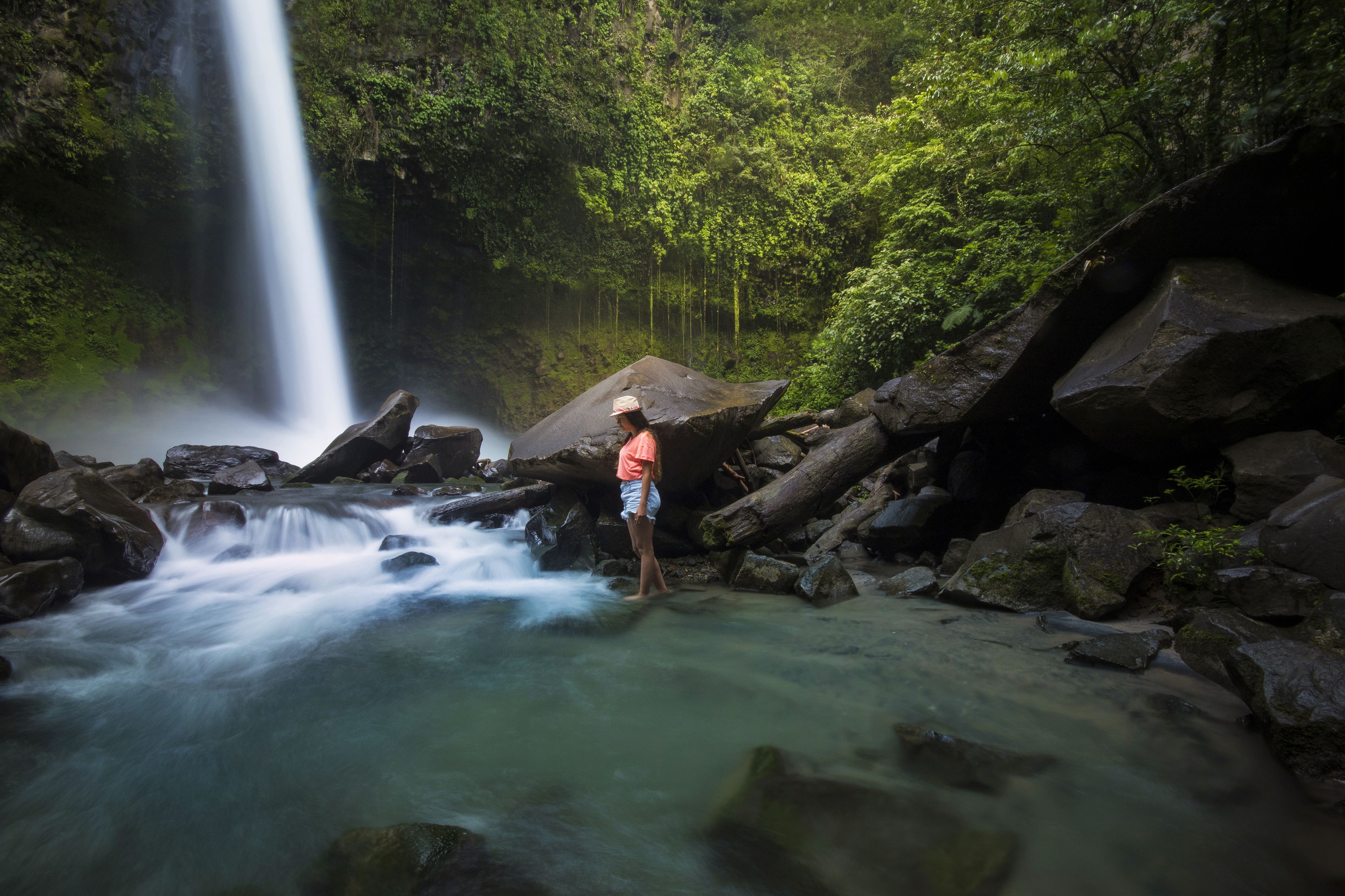 A waterfall in a forested area with rocks and a person standing near the water.