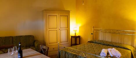 A room with a bed, a table with a bottle and glasses, a lamp, and a cabinet.