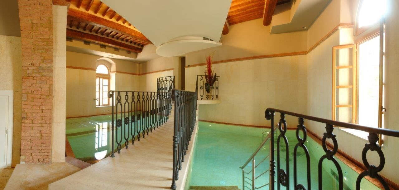 A staircase leading to a green pool area with a brick wall on the left and a wooden ceiling.