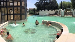 A swimming pool area with multiple pools, including a hot tub, surrounded by a building with large windows.
