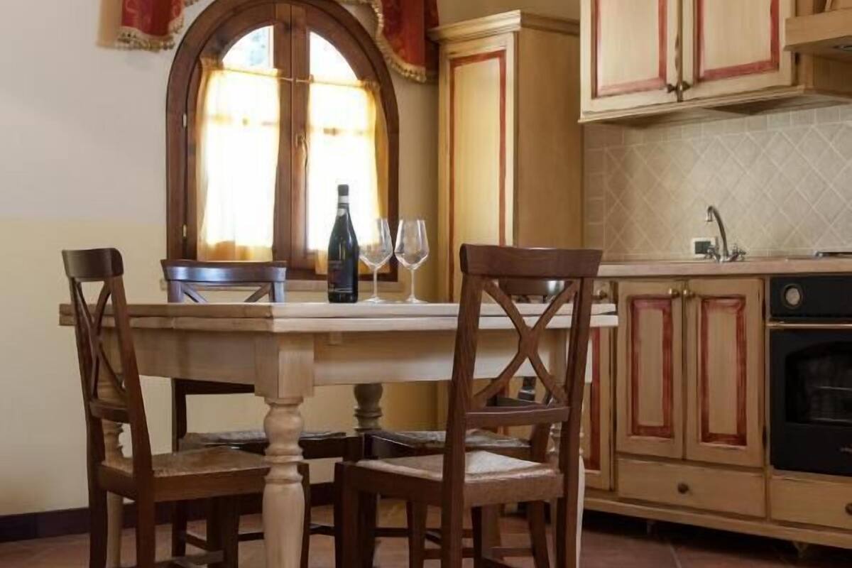 A dining area with a table and chairs, a window with curtains, and wooden cabinets.