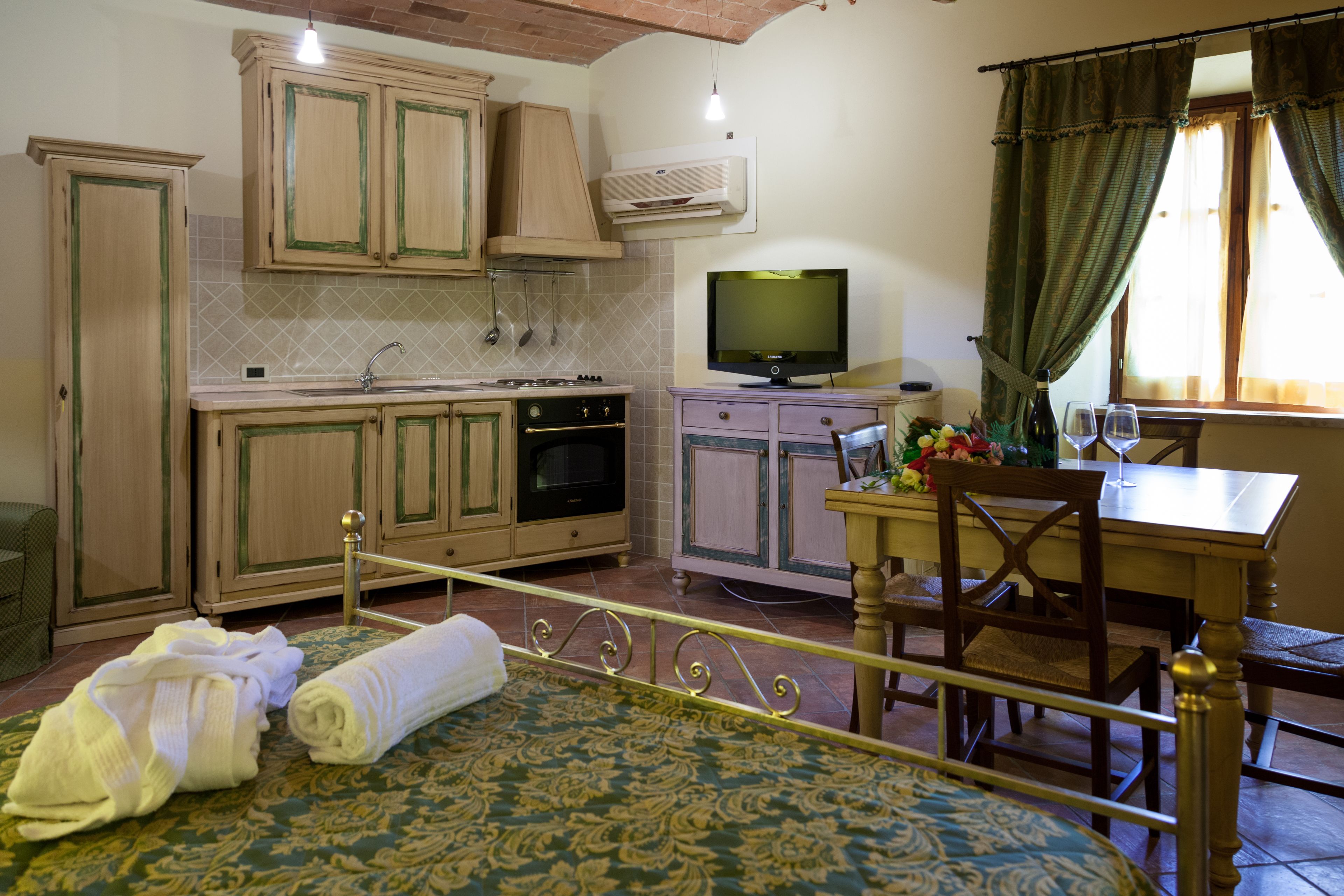 Une chambre d’hôtel comprenant un lit, une table à manger avec des chaises, un téléviseur et un coin cuisine avec des placards et une cuisinière.