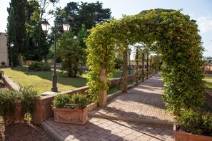 Un sendero pavimentado con borde de ladrillo, rodeado de follaje y una pared de ladrillo.