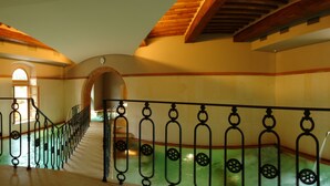 A grand staircase with ornate iron railings, leading to an upper level with arched doorways and a tiled floor.