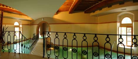 A grand staircase with ornate iron railings, leading to an upper level with arched doorways and a tiled floor.