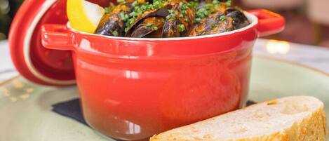 A red pot of mussels with a lemon wedge on a plate, accompanied by a piece of bread.